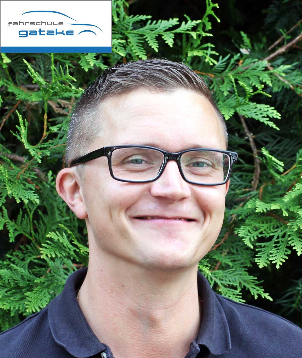 Ein lächelnder Mann mit Brille und kurzen Haaren vor grünem Hintergrund