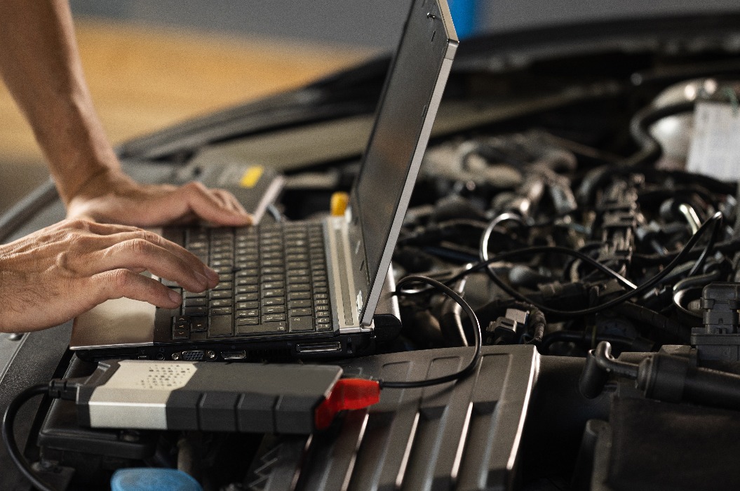 Ein Automechaniker benutzt einen Laptop, während er einen Diagnosetest durchführt. Moderner Autoservice. Computerdiagnose des Autos. Ein europäischer Automechaniker hält ein digitales Gerät